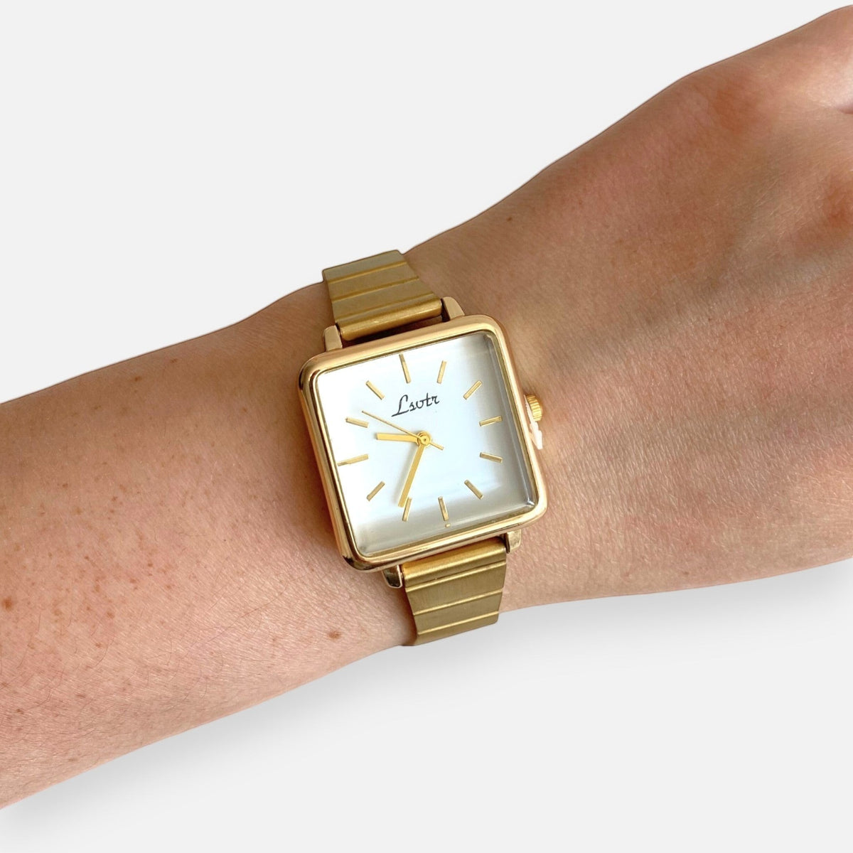 Reloj Hv Hermanas Villegas de caja cuadrada dorada, dial blanco y correa metálica extensible de estilo vintage.