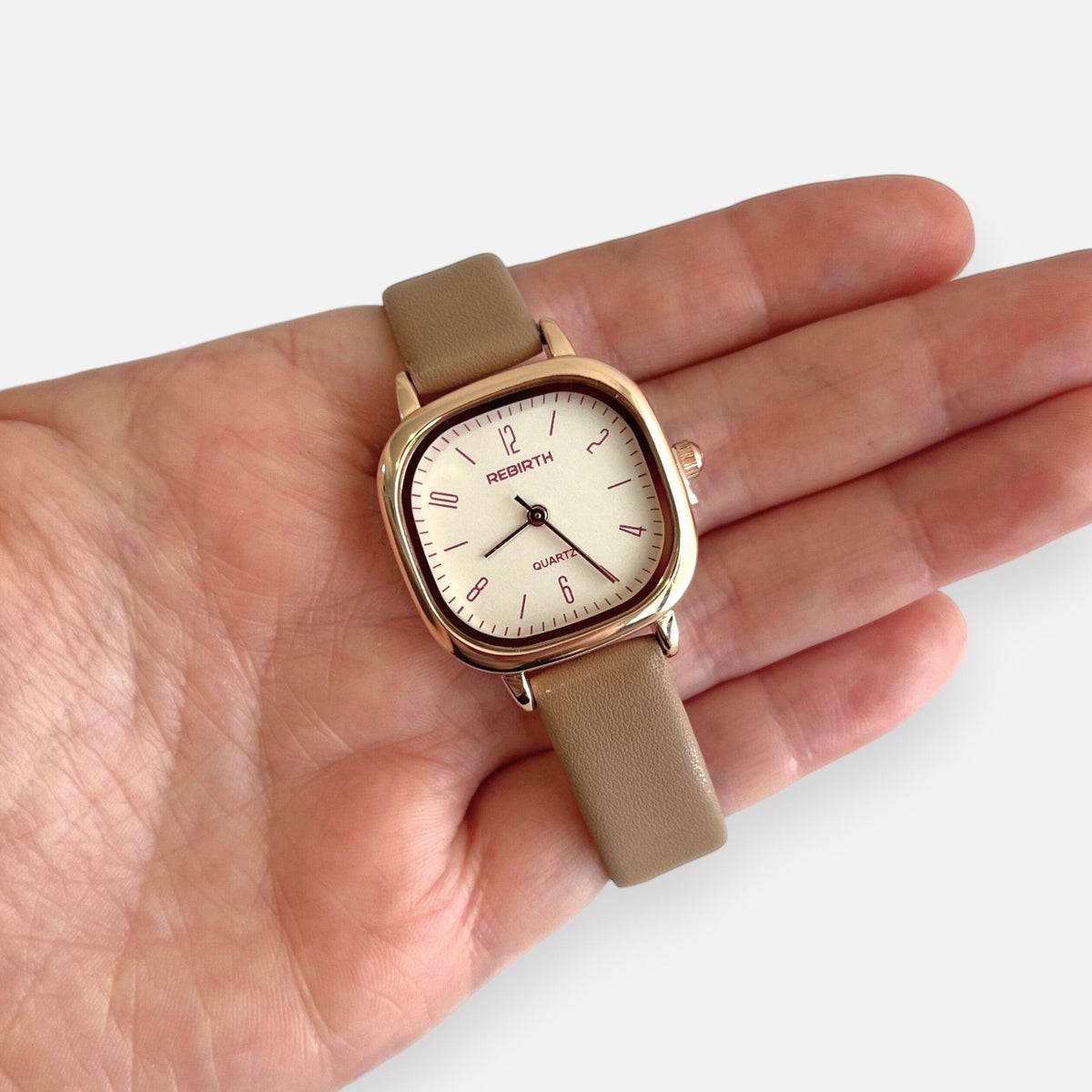 Reloj Hv Hermanas Villegas con caja cuadrada oro rosa, dial claro y correa de cuero vegano beige en una mano