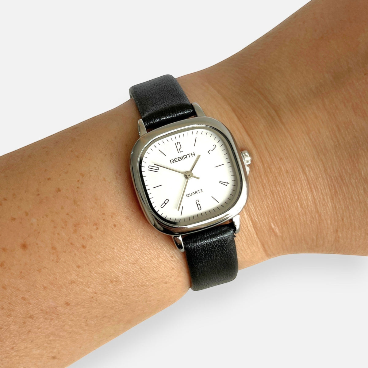 Reloj Hv Hermanas Villegas con caja cuadrada plateada, dial blanco y correa de cuero vegano negro en la muñeca