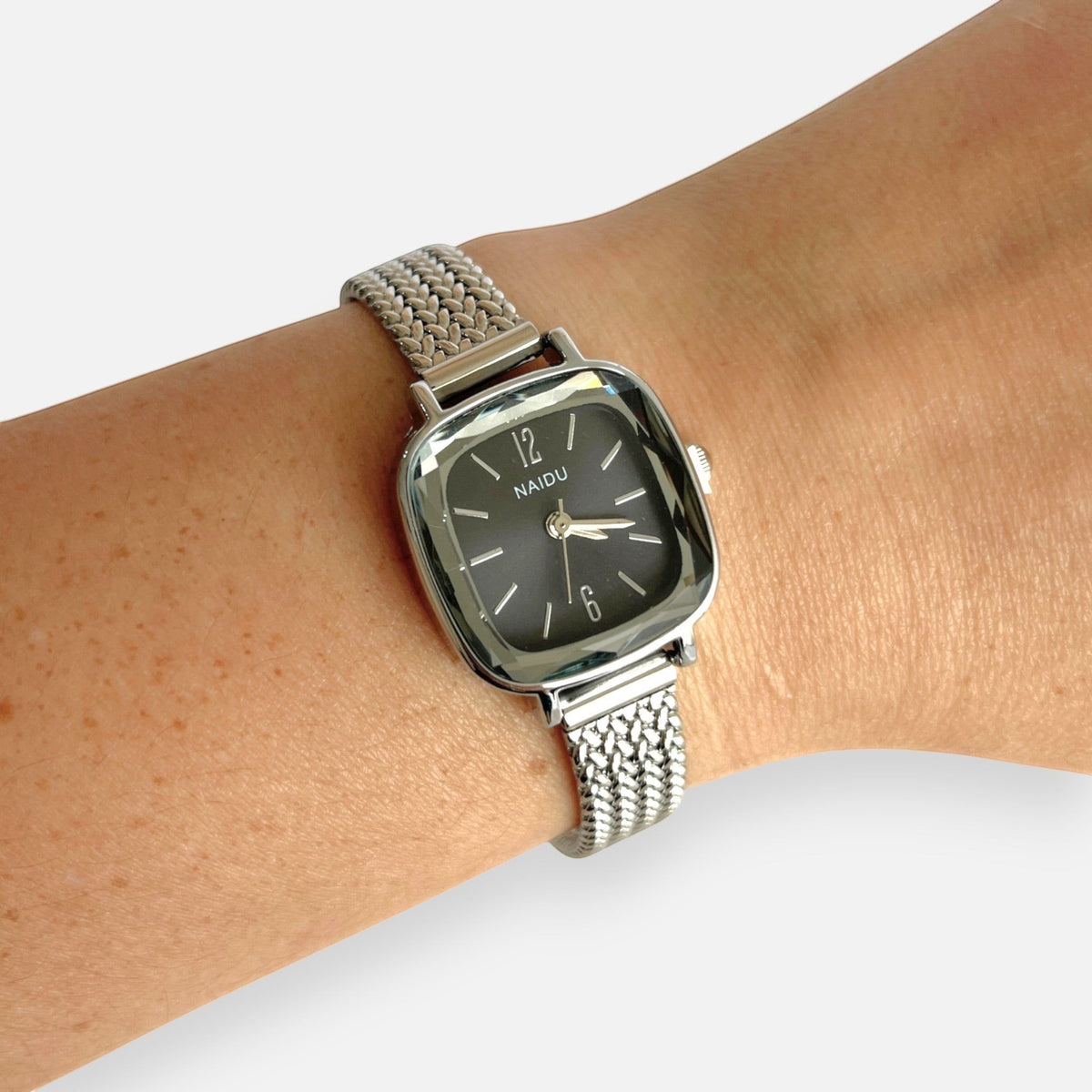 Reloj Hv Hermanas Villegas de caja cuadrada plateada, dial negro y correa de acero inoxidable con diseño trenzado.