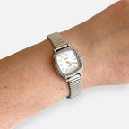 Reloj Hv Hermanas Villegas cuadrado plateado con bisel labrado, dial blanco y números romanos en una muñeca