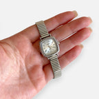 Reloj Hv Hermanas Villegas plateado de caja cuadrada con bisel labrado, dial blanco y números romanos en una mano