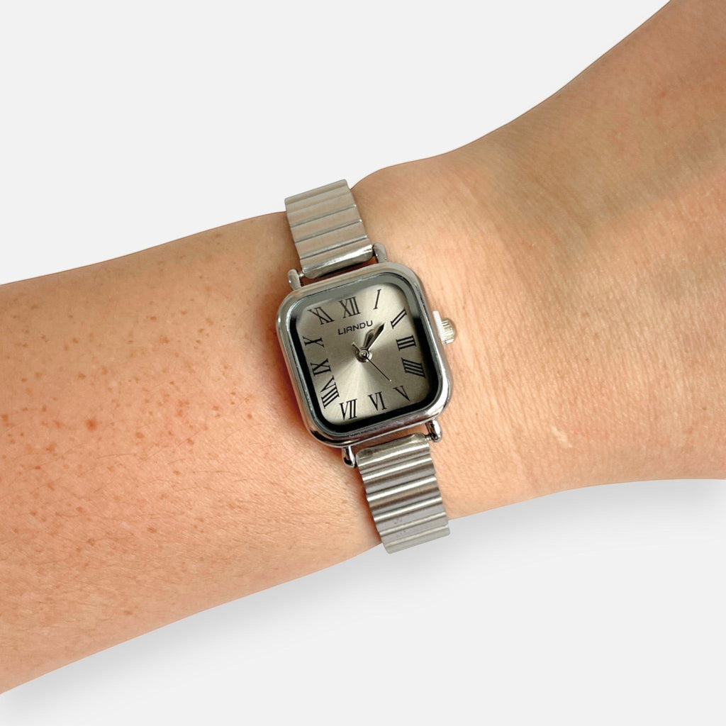 Reloj Hv Hermanas Villegas de caja cuadrada plateada, dial champán con números romanos y correa extensible flexible.
