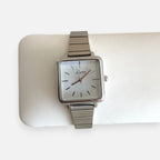 Reloj Hv Hermanas Villegas de caja cuadrada plateada, dial blanco y correa metálica extensible estilo vintage.