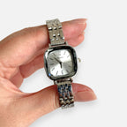 Reloj analógico Hv Hermanas Villegas de acero plateado con caja cuadrada, dial minimalista y correa de eslabones.