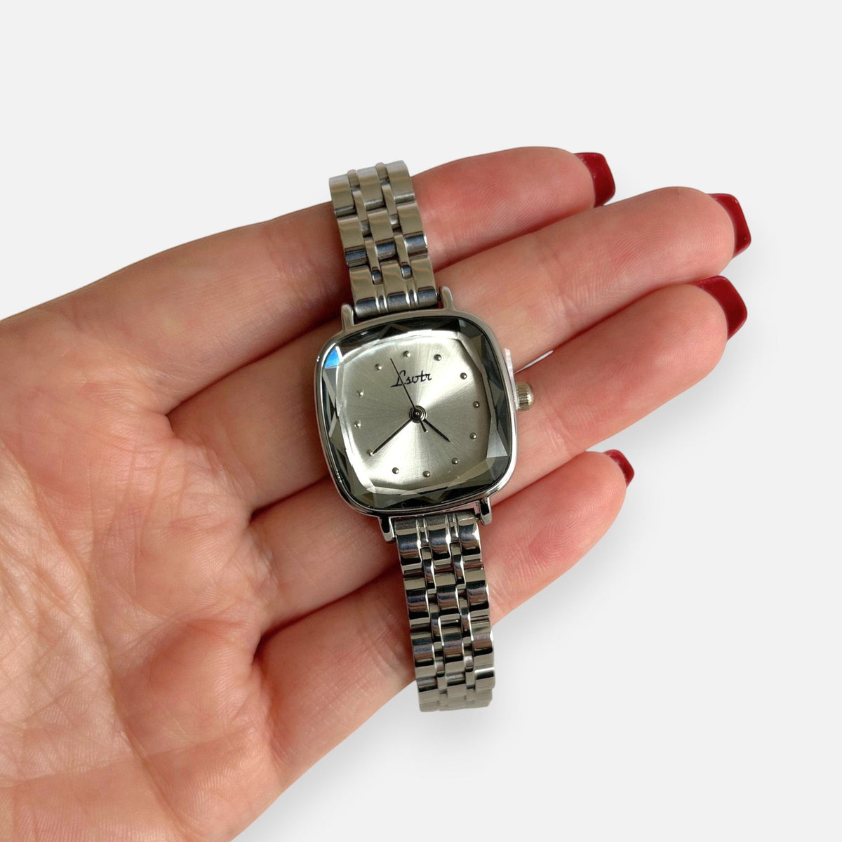 Reloj Hv Hermanas Villegas plateado con caja cuadrada, cristal biselado y correa de acero en mano femenina.