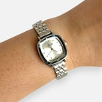 Reloj Hv Hermanas Villegas plateado con caja cuadrada, cristal biselado y correa de acero en muñeca femenina