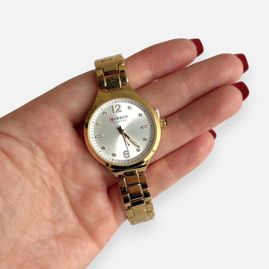 Reloj Hv Hermanas Villegas dorado de acero con dial satinado, números aplicados y detalles de circones en la mano