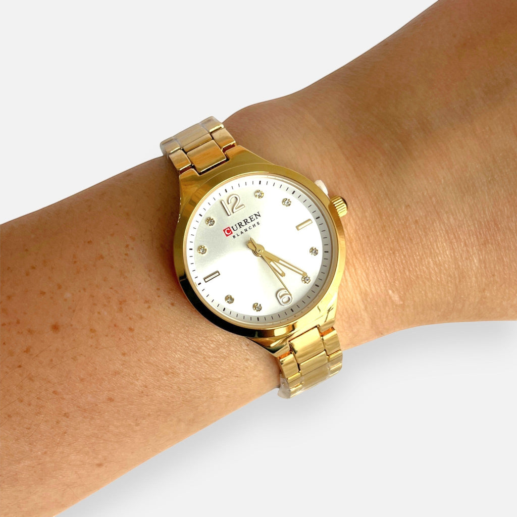 Reloj analógico Hv Hermanas Villegas dorado con correa de acero, dial claro y marcadores de circones en muñeca