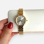 Reloj analógico Hv Hermanas Villegas dorado con caja redonda, dial satinado, cuatro circones y correa de acero fino.