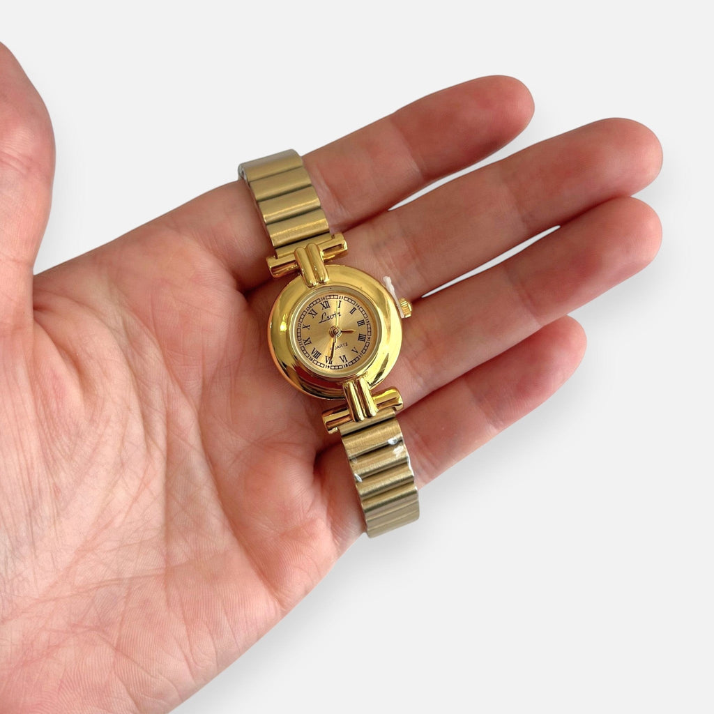 Reloj analógico Hv Hermanas Villegas de acero dorado con caja redonda, números romanos y correa de eslabones flexible.