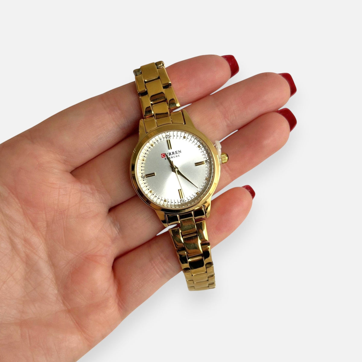 Reloj analógico Hv Hermanas Villegas dorado con correa de acero, dial satinado y detalles de circones en la mano