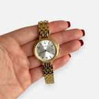 Reloj Hv Hermanas Villegas dorado con dial plateado, circones y correa de acero en mano femenina