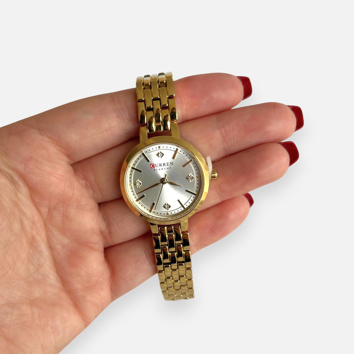 Reloj Hv Hermanas Villegas dorado con dial plateado, circones y correa de acero en mano femenina