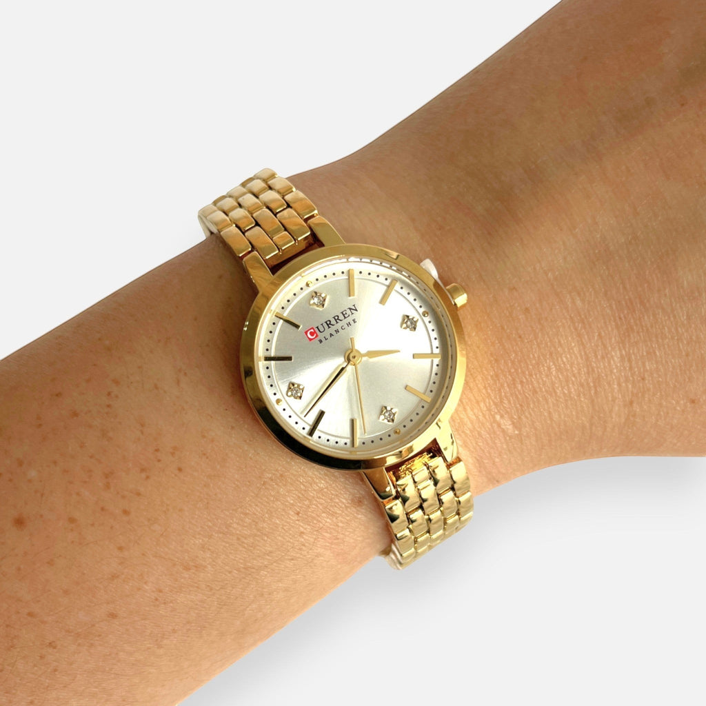 Reloj analógico Hv Hermanas Villegas dorado con caja redonda, dial claro y detalles de circones en correa de acero