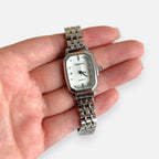 Reloj analógico Hv Hermanas Villegas de acero plateado con caja octagonal, dial claro y detalles brillantes.