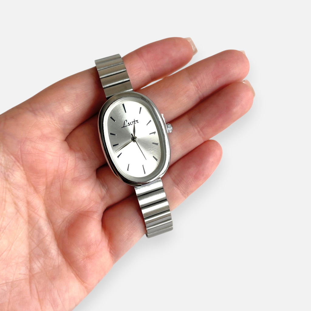 Reloj Hv Hermanas Villegas ovalado de acero plateado con correa de eslabones y dial minimalista en mano