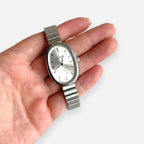 Reloj Hv Hermanas Villegas ovalado de acero plateado con correa de eslabones y dial minimalista en mano