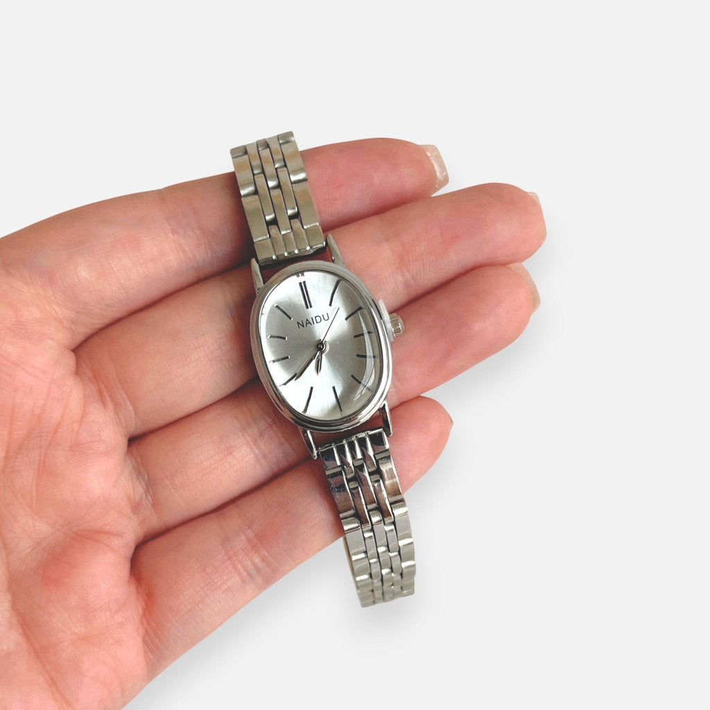 Reloj analógico Hv Hermanas Villegas con caja ovalada plateada, dial satinado y correa de acero inoxidable