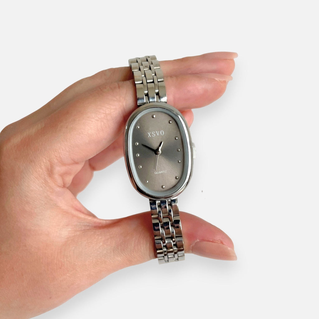 Reloj analógico Hv Hermanas Villegas con caja ovalada plateada, dial gris topo y correa de acero inoxidable pulido