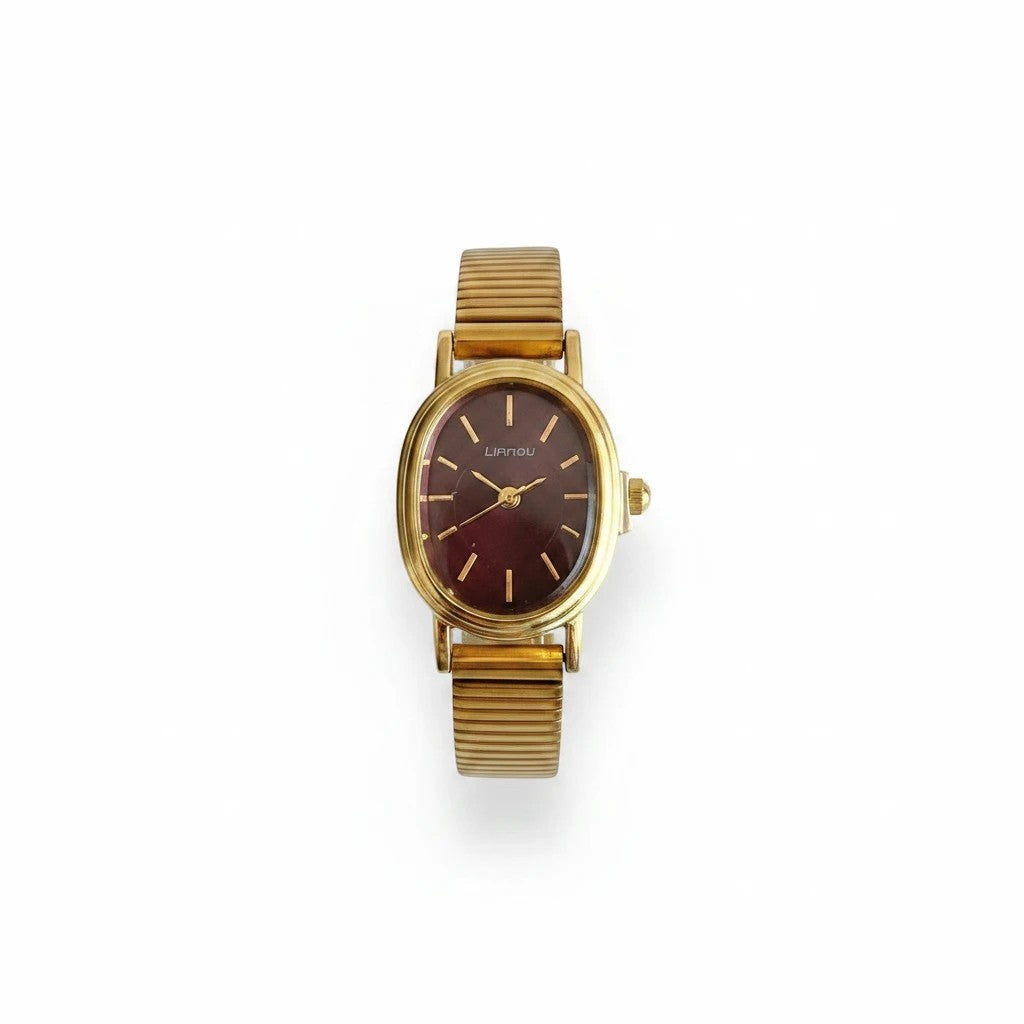 Reloj Hv Hermanas Villegas ovalado con caja dorada, dial guinda y correa metálica extensible de estilo vintage.