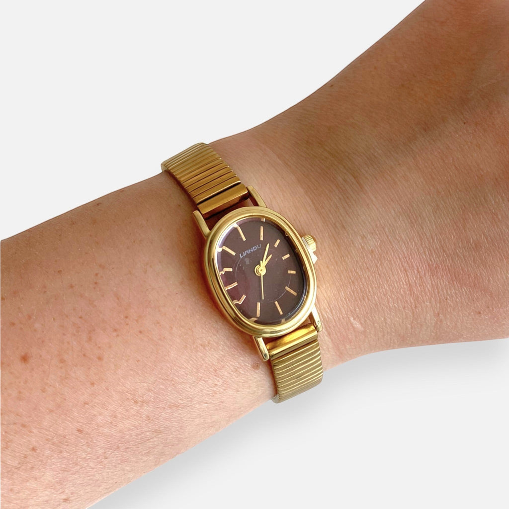Reloj Hv Hermanas Villegas ovalado dorado con dial guinda y correa metálica extensible de estilo vintage en muñeca