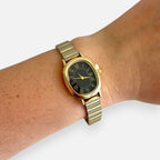 Reloj Hv Hermanas Villegas ovalado dorado con dial negro, números romanos y correa extensible en muñeca
