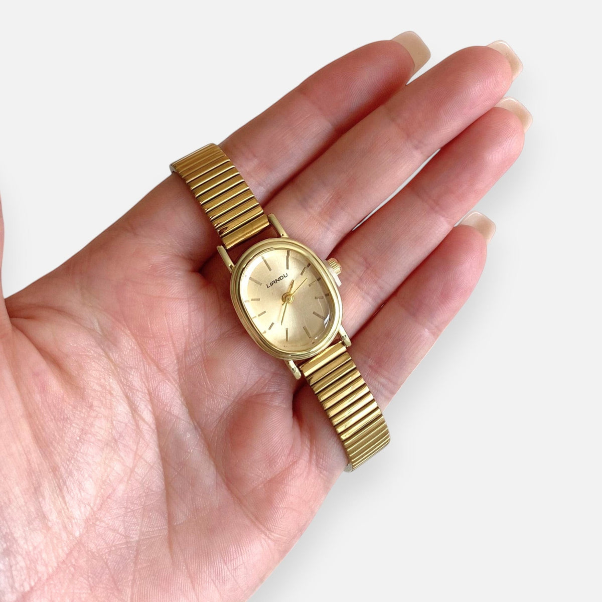 Reloj Hv Hermanas Villegas ovalado dorado con correa extensible metálica y dial minimalista en mano femenina