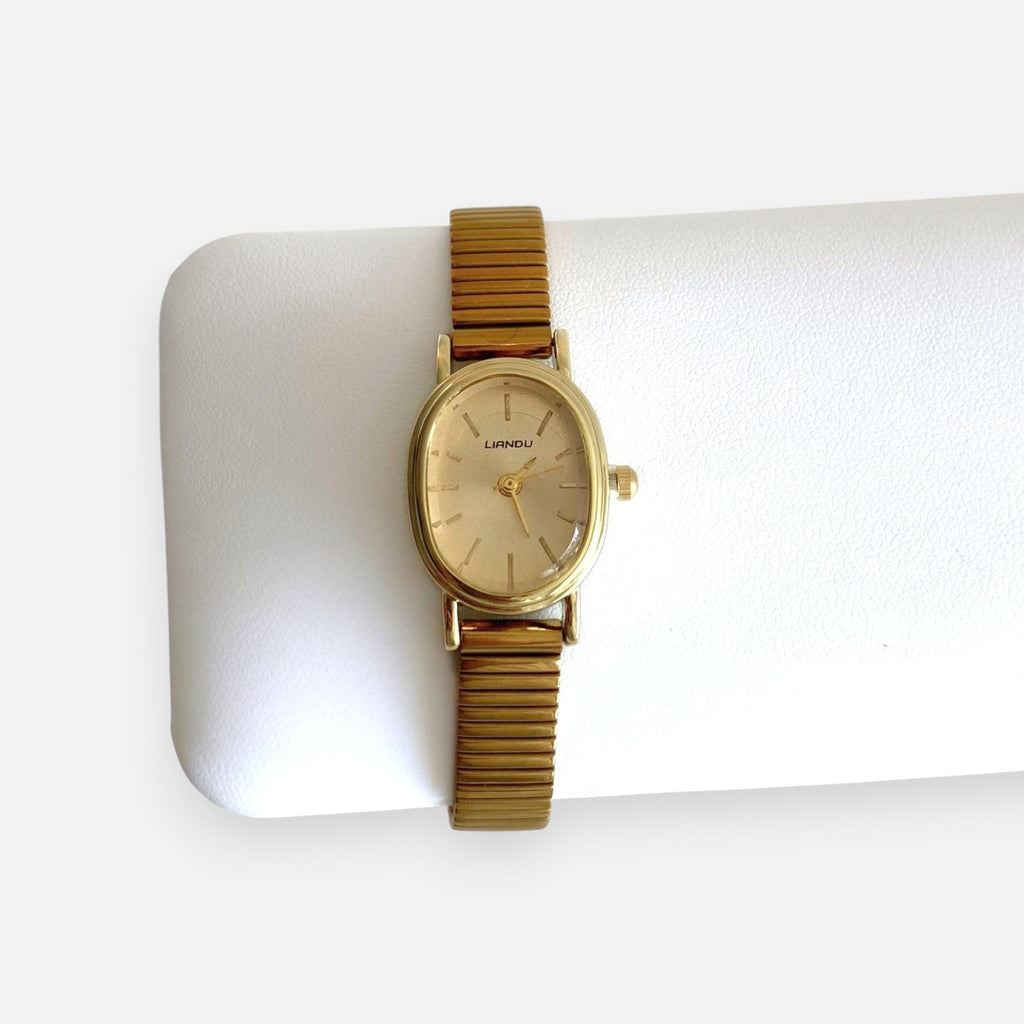Reloj analógico Hv Hermanas Villegas con caja ovalada dorada, dial cepillado y correa metálica extensible vintage.