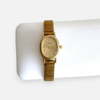 Reloj analógico Hv Hermanas Villegas con caja ovalada dorada, dial cepillado y correa metálica extensible vintage.