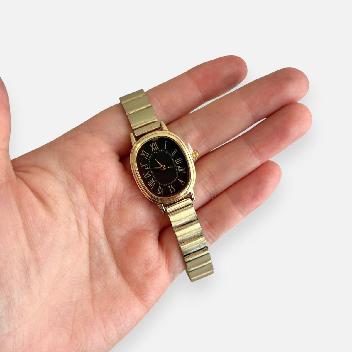 Reloj Hv Hermanas Villegas ovalado dorado con dial negro y números romanos en mano