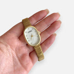 Reloj Hv Hermanas Villegas ovalado dorado con dial nacarado, marcadores de circones y correa extensible flexible.
