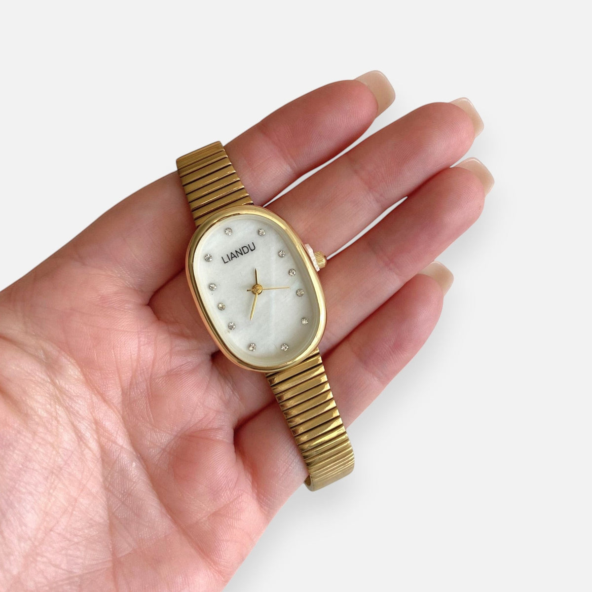 Reloj Hv Hermanas Villegas ovalado dorado con dial nacarado, marcadores de circones y correa extensible flexible.