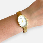 Reloj Hv Hermanas Villegas ovalado dorado con dial nacarado y marcadores de cristales en muñeca femenina