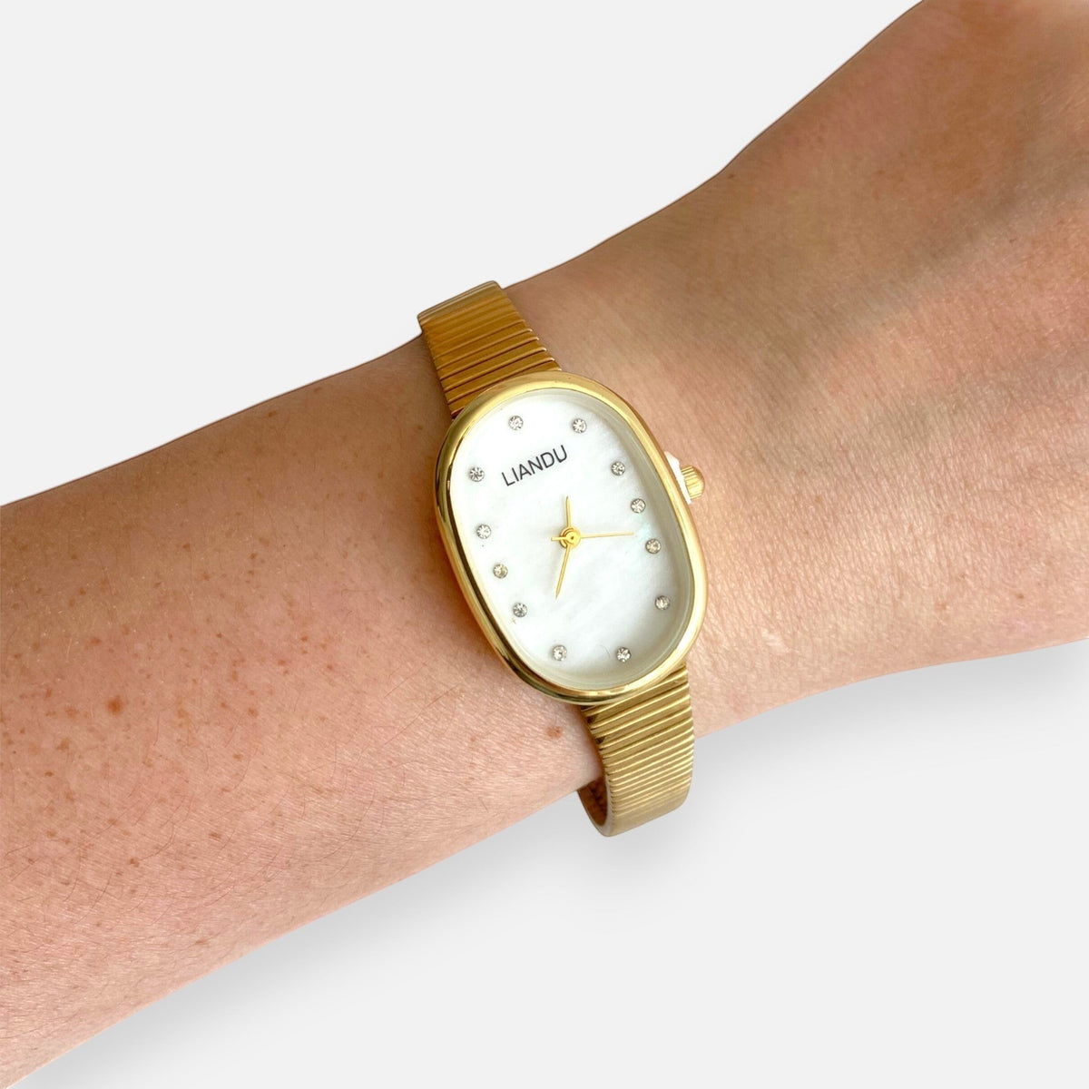 Reloj Hv Hermanas Villegas ovalado dorado con dial nacarado y marcadores de cristales en muñeca femenina