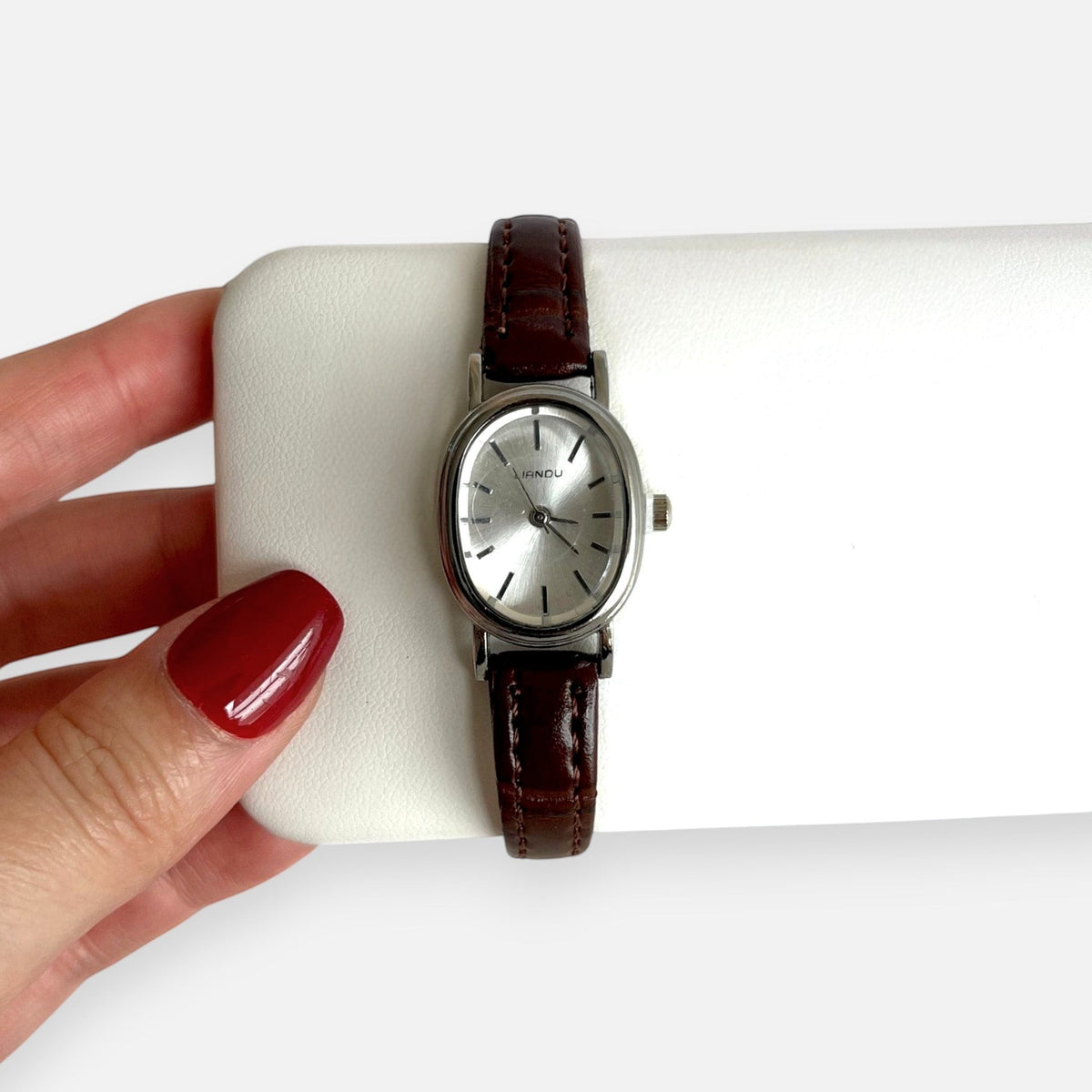 Reloj Hv Hermanas Villegas con caja ovalada plateada, dial minimalista y correa de cuero vegano café estilo vintage