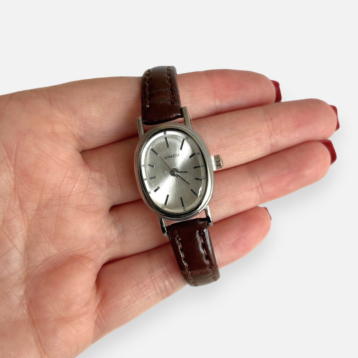 Reloj Hv Hermanas Villegas ovalado plateado con dial satinado y correa de cuero vegano café en mano