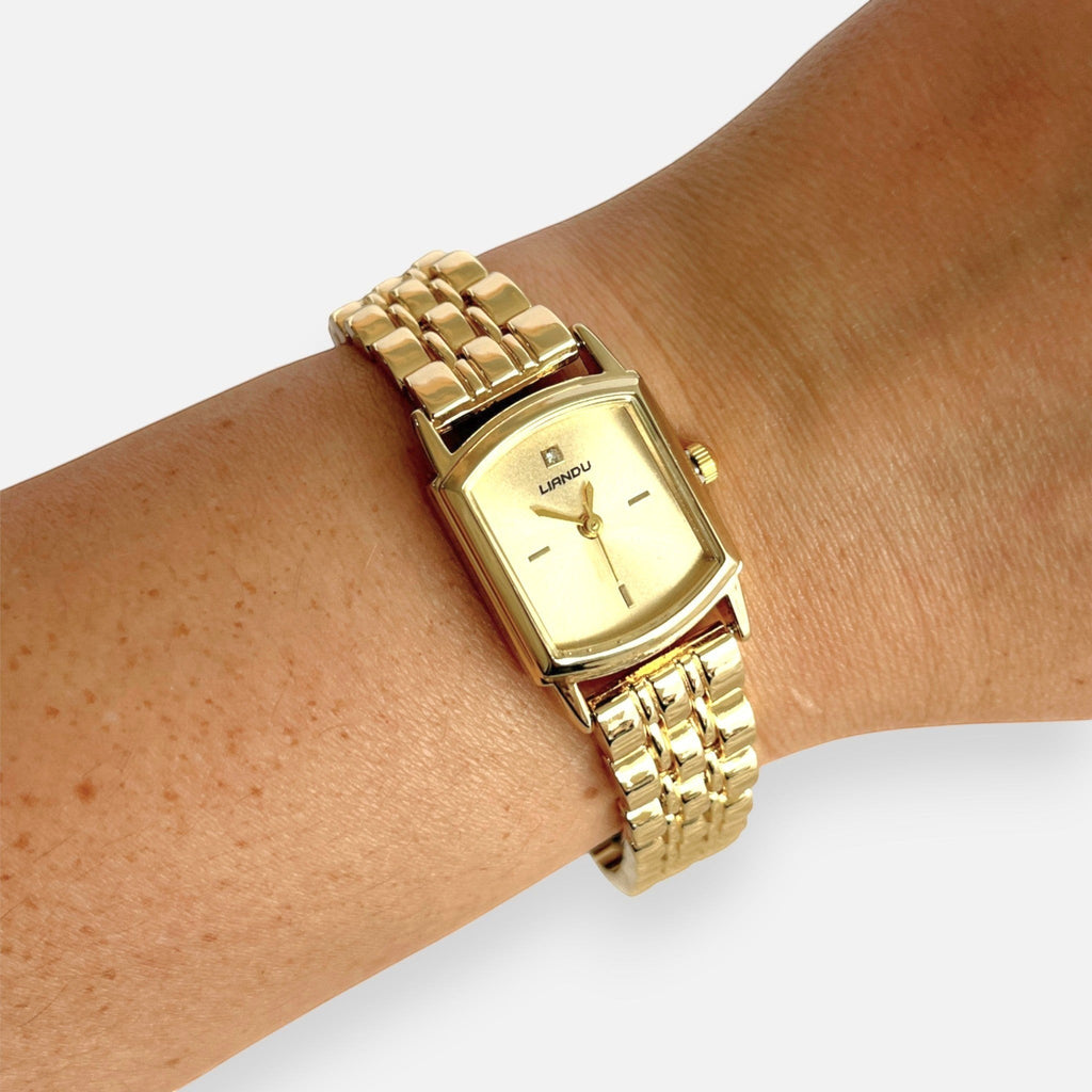 Reloj Hv Hermanas Villegas rectangular dorado con correa de acero, dial satinado y detalle de circon en la muñeca.
