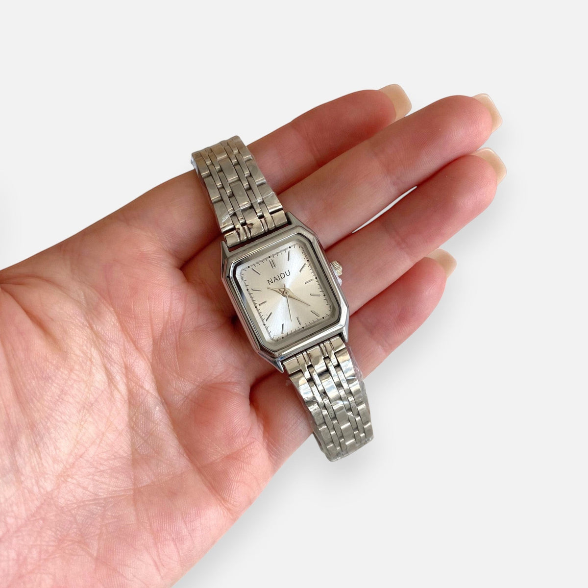 Reloj Hv Hermanas Villegas rectangular plateado en acero con dial satinado y correa de eslabones sobre una mano