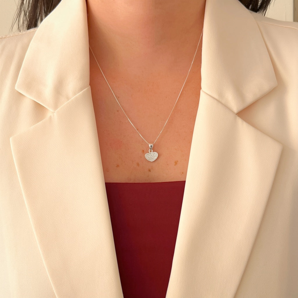Set de joyería Hv Hermanas Villegas en plata 925 con collar de dije corazón pavé y aretes a juego sobre blazer beige